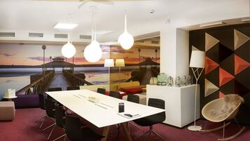 A modern conference room with a large table, black chairs, and a mural of a sunset over water.