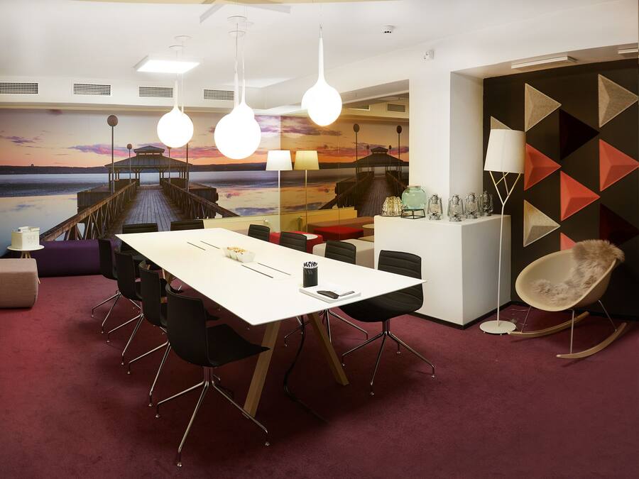 A modern conference room with a large table, black chairs, and a mural of a sunset over water.