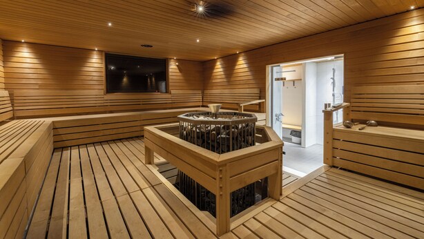 Un sauna avec des lambris en bois aux murs et au plafond, un banc central en bois et une petite table équipée d’un radiateur.