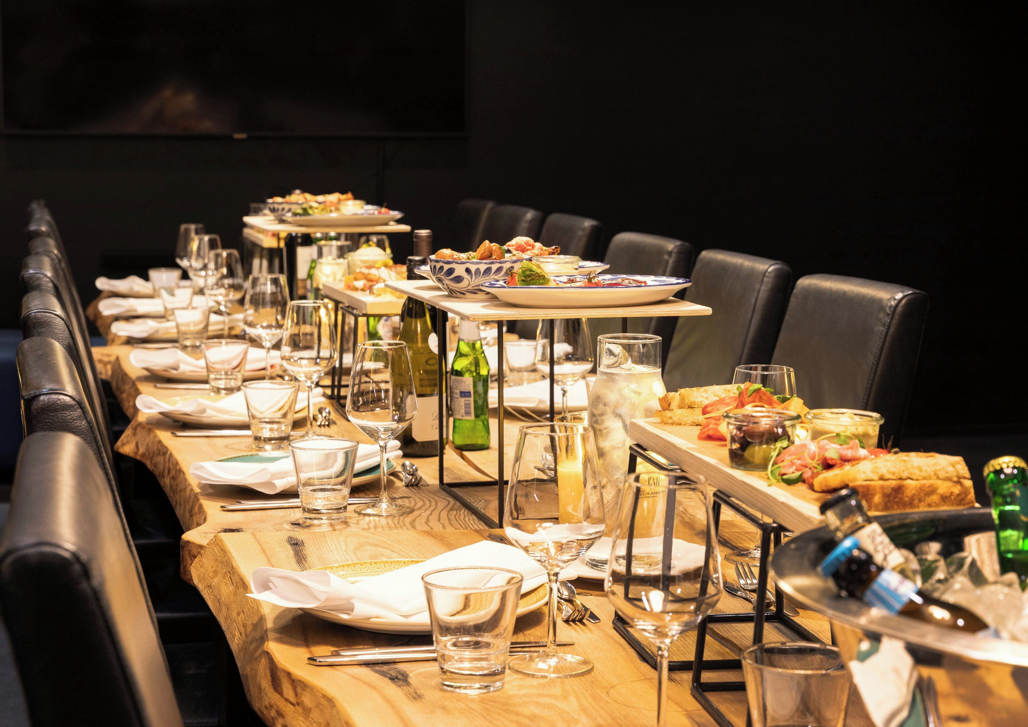 A long dining table set with multiple plates of food, glasses, and bottles, indicating a restaurant setting.