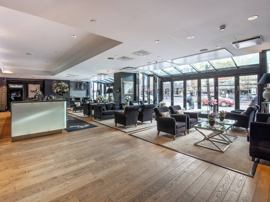 Een ruime lobby met een receptiebalie, een comfortabele zithoek en grote ramen met uitzicht op de straat.