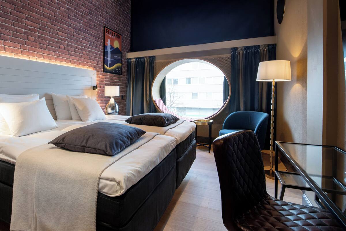 Una habitación de hotel con una cama, un espejo redondo, una silla y una lámpara.