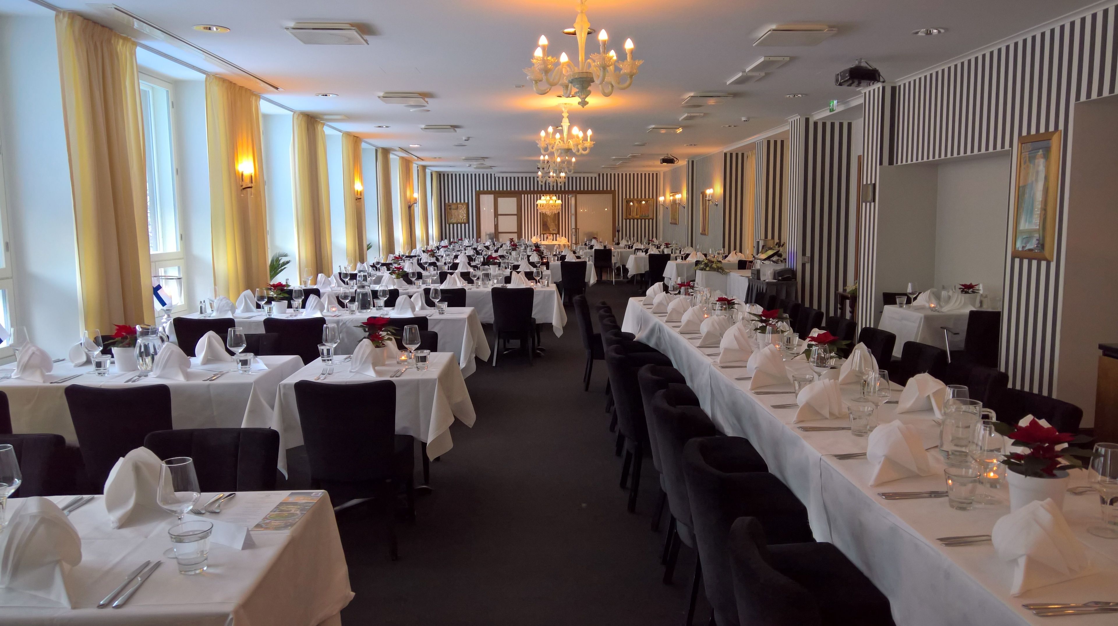 A long dining hall with tables set for a formal event, featuring chandeliers and striped wallpaper.