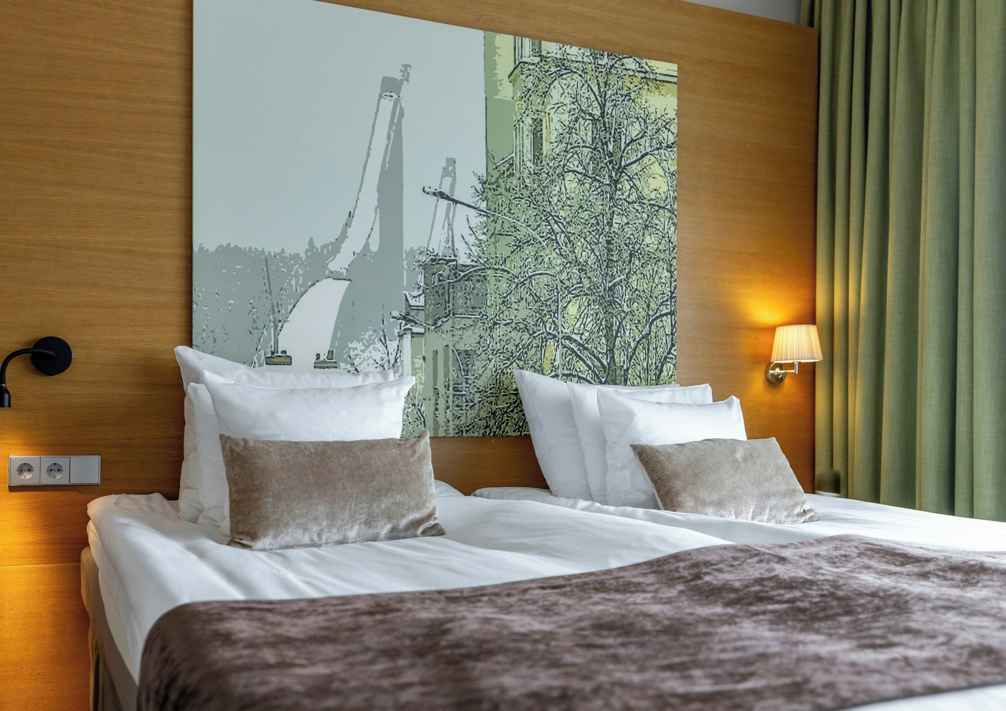 A hotel room with a bed, pillows, a blanket, a wall-mounted lamp, and a painting.