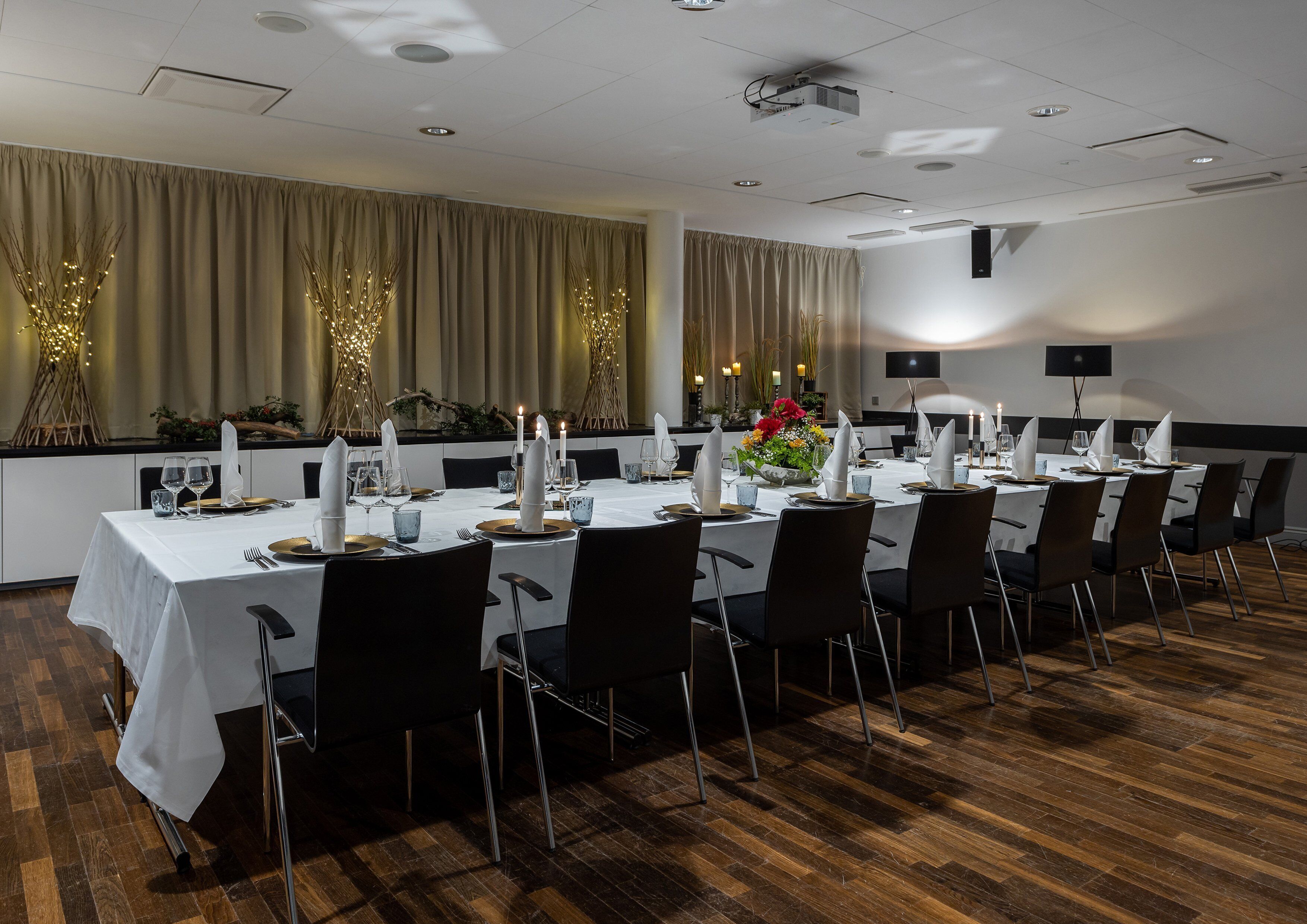 Un salón de conferencias bien iluminado con una larga mesa dispuesta para una reunión, que incluye un proyector y una televisión de pantalla plana en la pared.