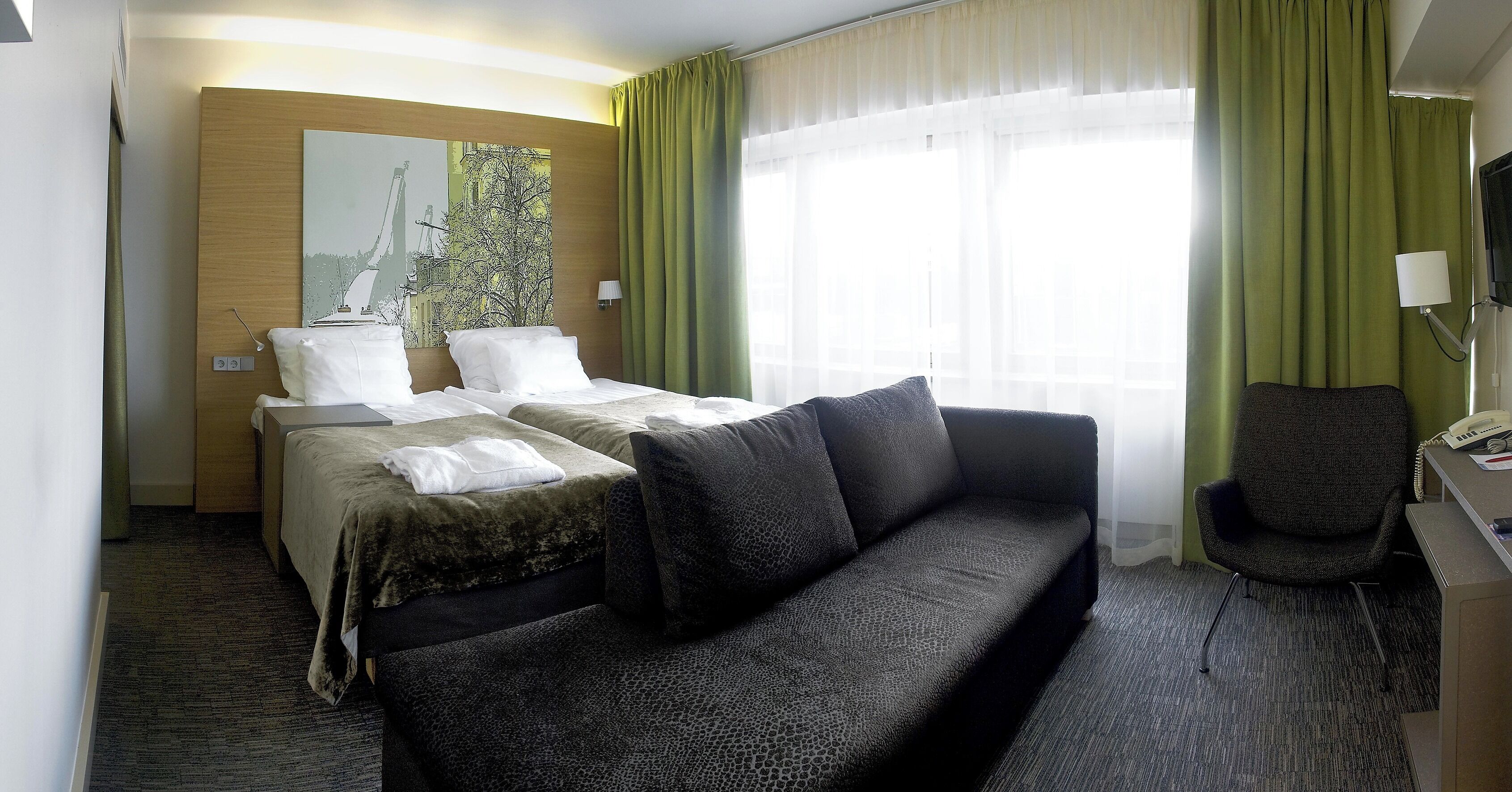 Habitación de hotel con dos camas, un sofá, un escritorio con teléfono y un cuadro en la pared.