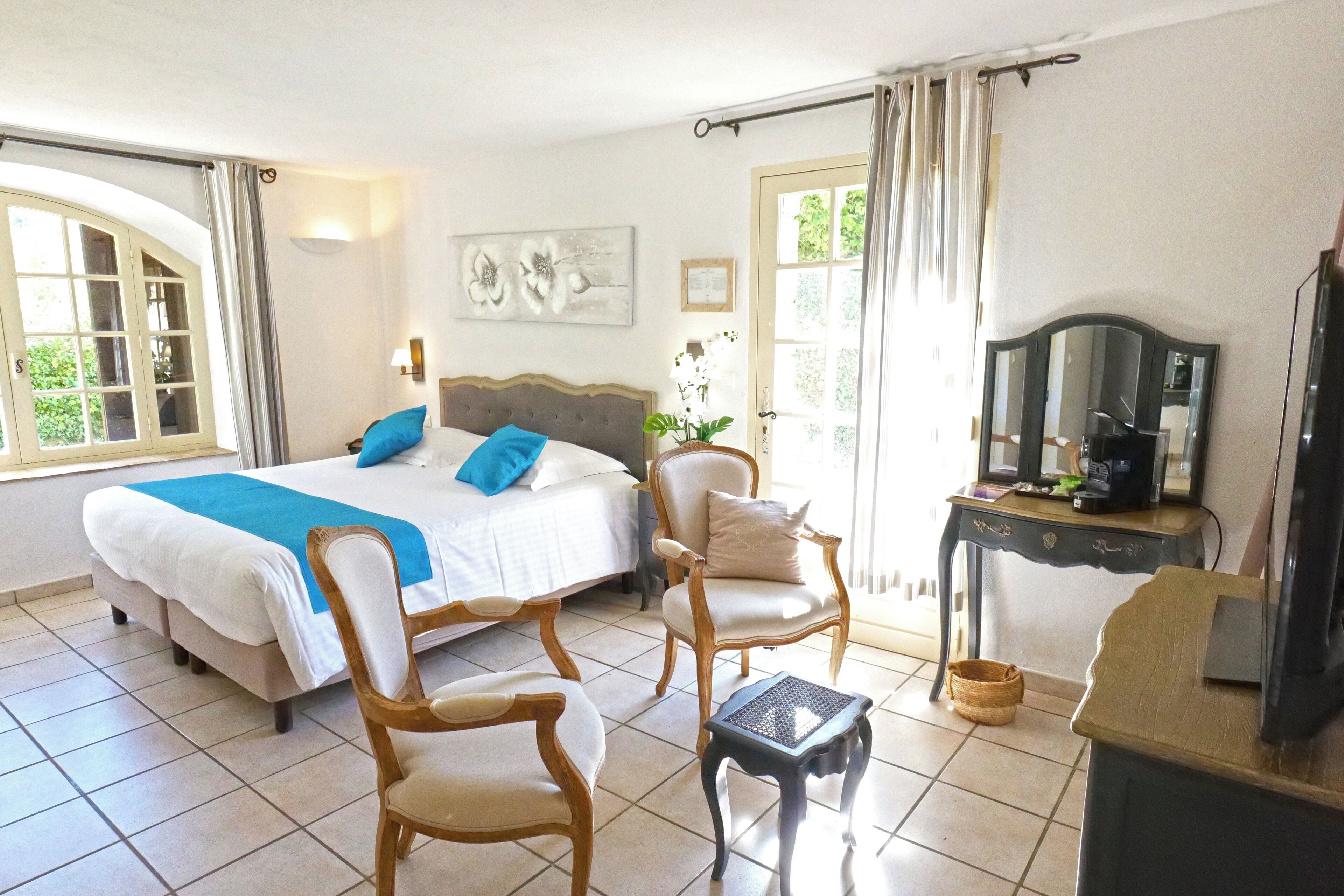 A hotel room with a bed, two chairs, a small table, a mirror, and a television.