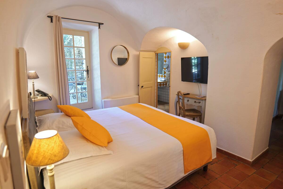 A bedroom with a bed, a lamp, a TV, a door, and a window.