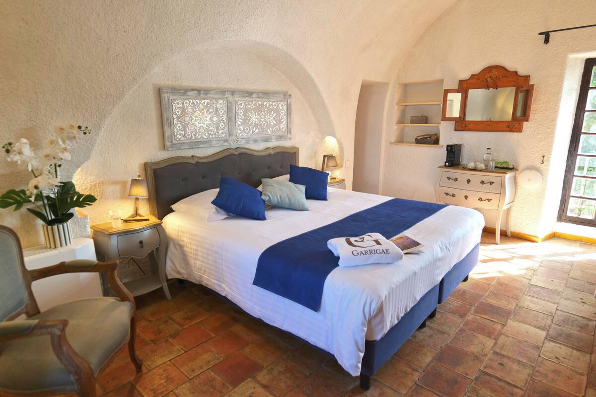 A bedroom with a large bed, a nightstand with a lamp, a dresser, and a mirror.