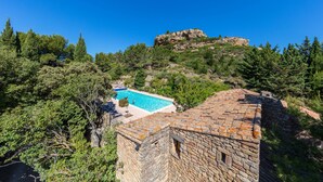 Edifici de pedra amb una piscina, envoltat d'arbres i un turó rocos.