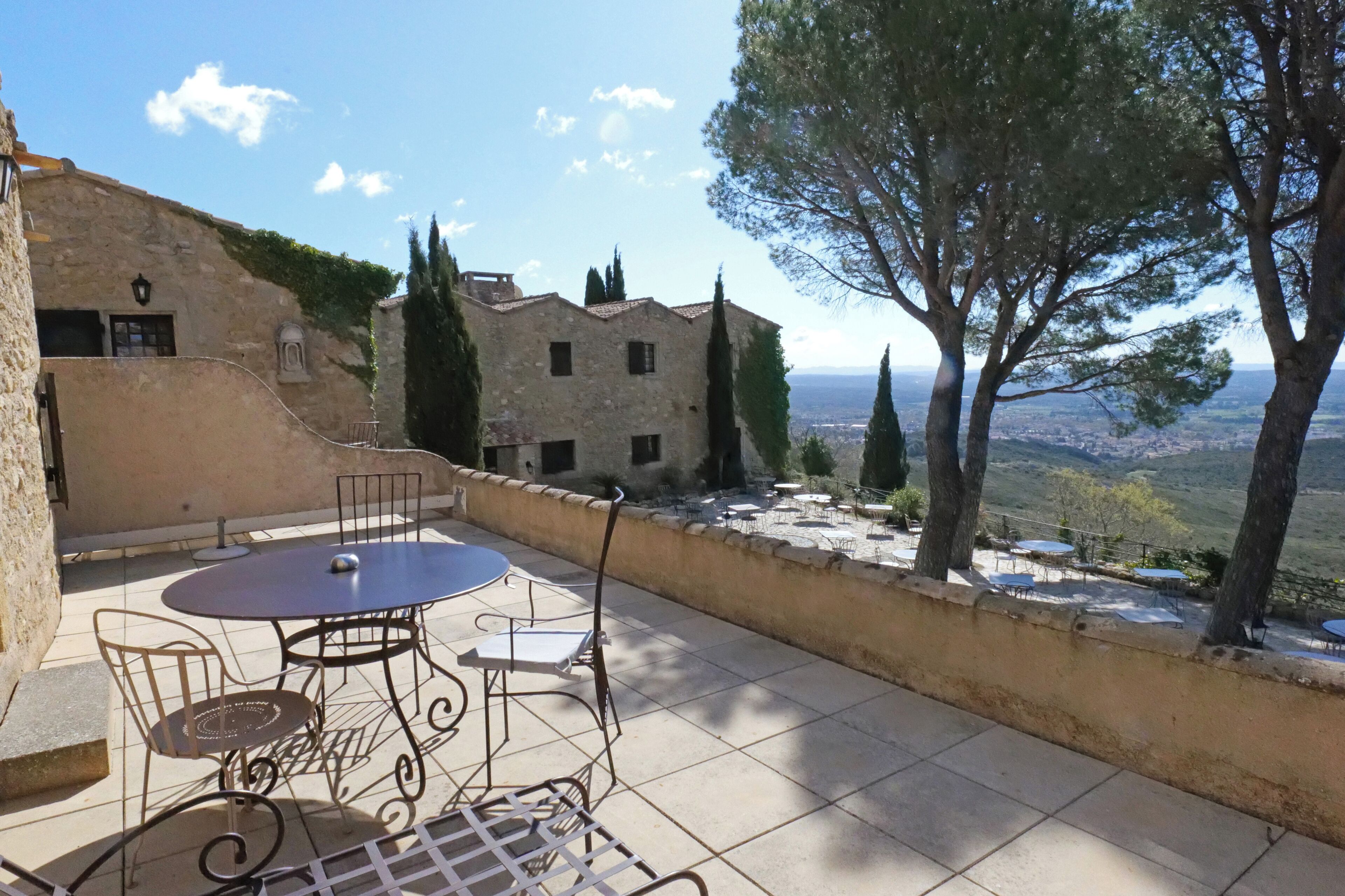 Une terrasse avec une table ronde et des chaises, un bâtiment en pierre et une vue sur le paysage.