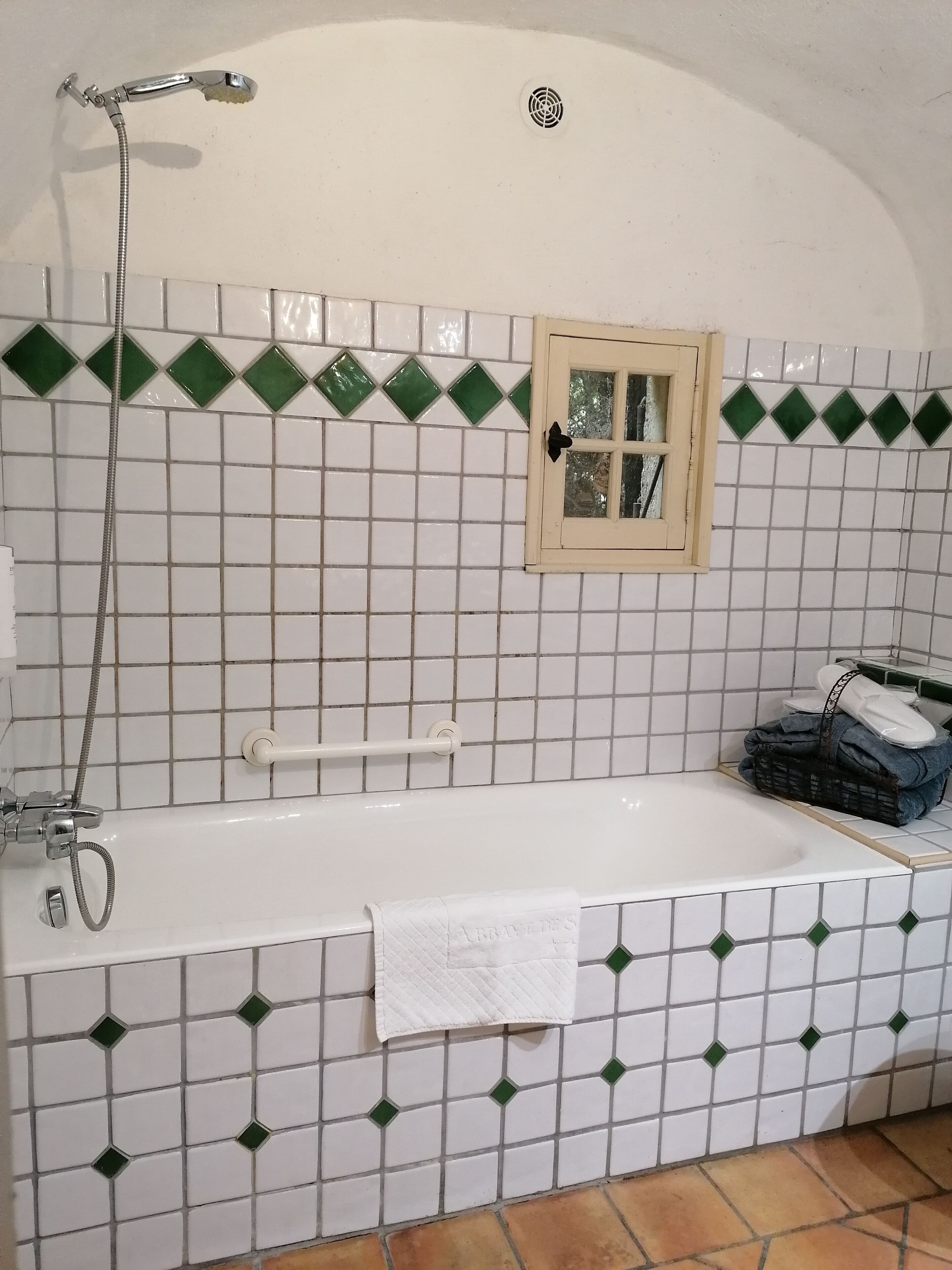 Een badkamer met een witte badkuip, een douche en een raam met houten kader.