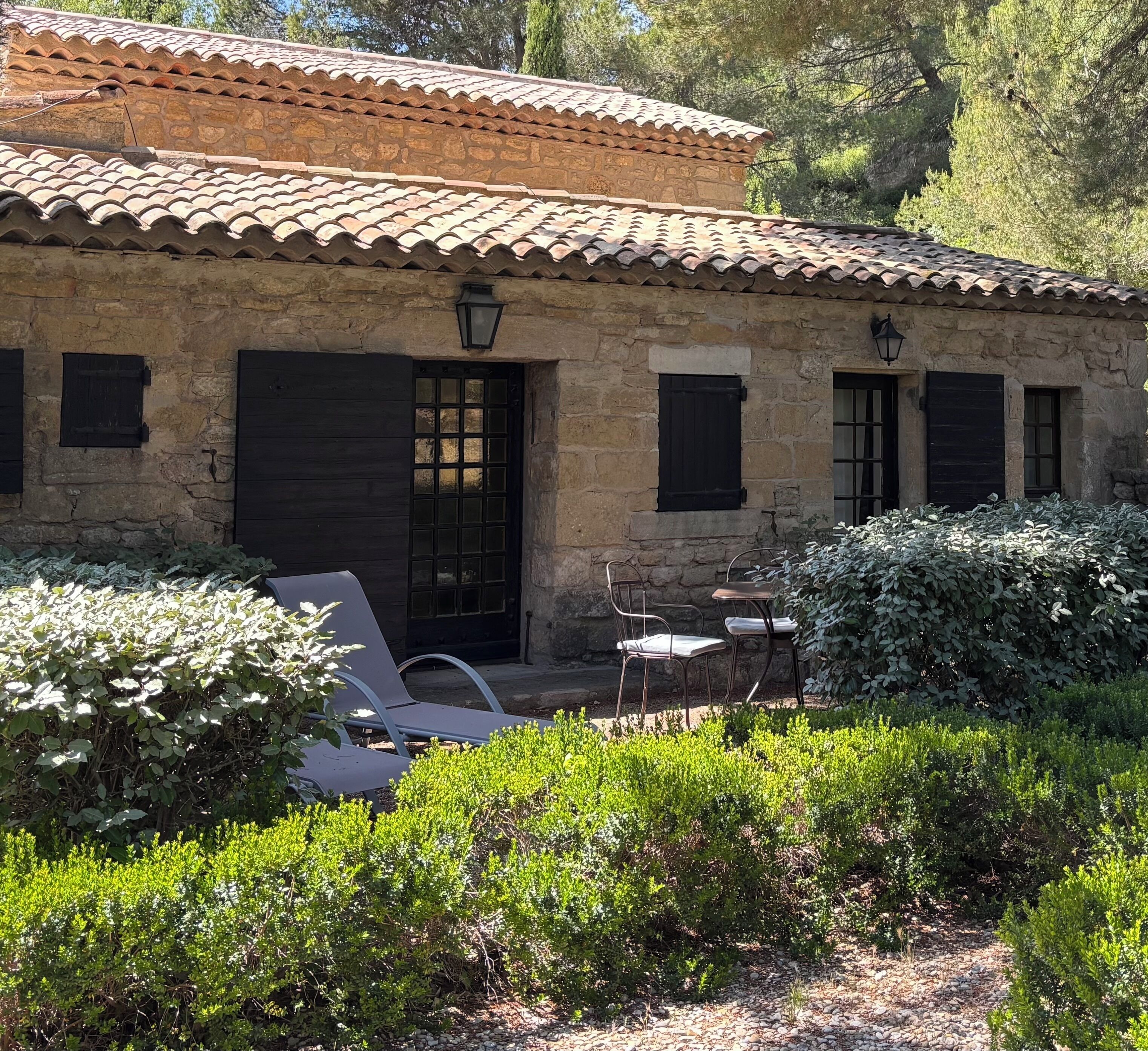 A stone building with a tiled roof, a door, and windows. There are outdoor chairs and a table.