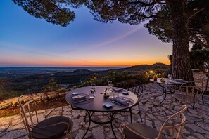 An outdoor dining area with a table set for two, overlooking a scenic landscape during sunset. - Garrigae Abbaye de Sainte Croix (Salon-de-Provence)