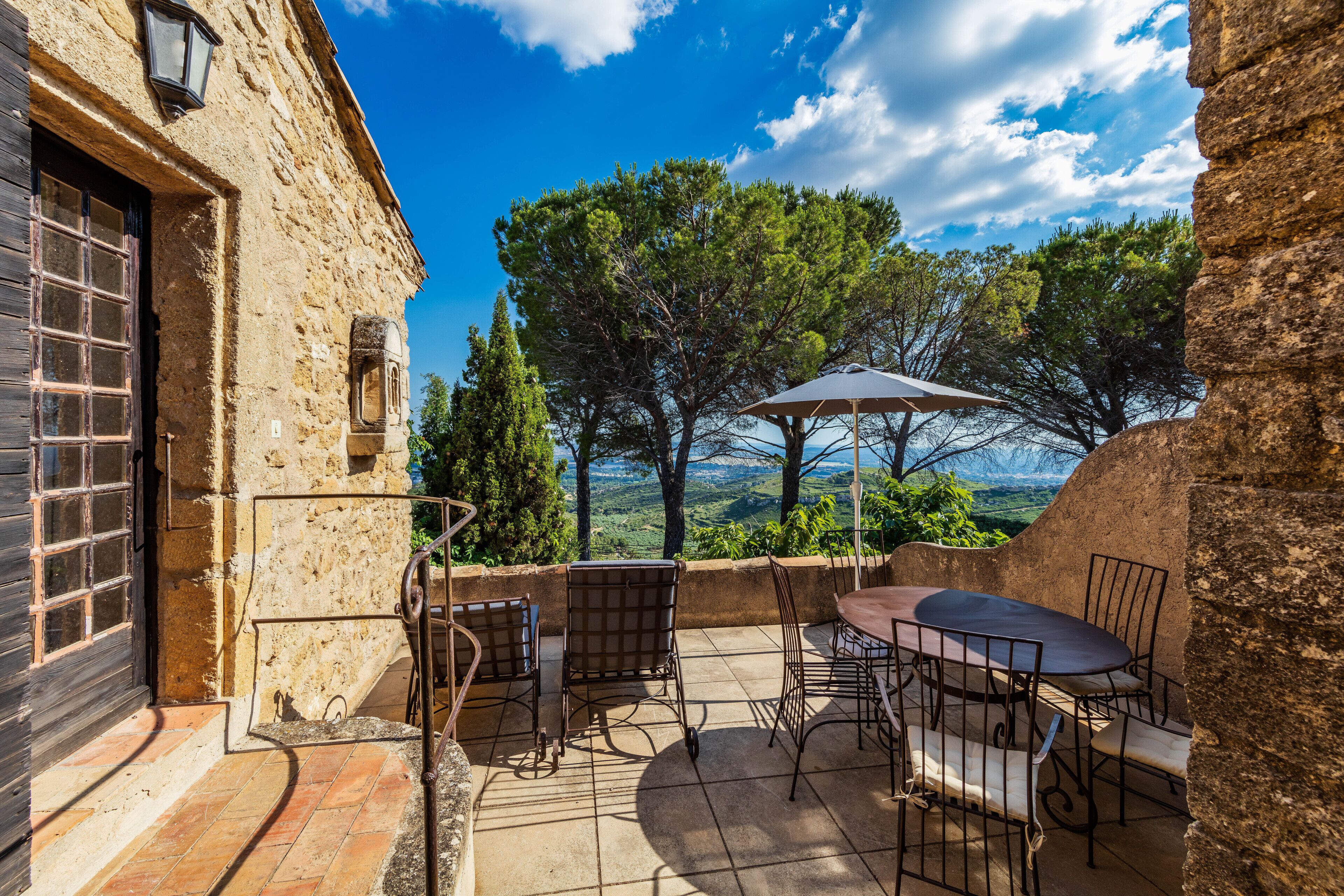 Une terrasse extérieure avec des murs en pierre, une table, des chaises et une vue sur le paysage.