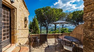 Une terrasse extérieure avec des murs en pierre, une table, des chaises et une vue sur le paysage.