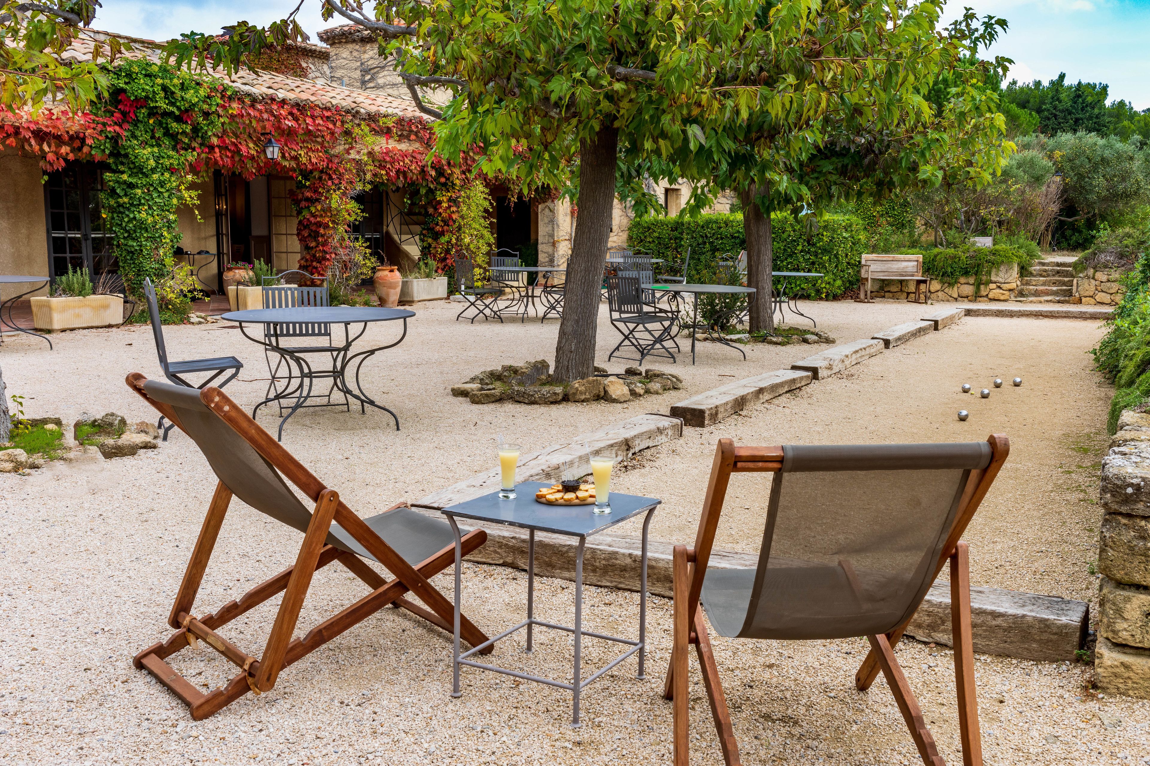 An outdoor seating area with tables and chairs, surrounded by a garden with a stone wall and a tree.