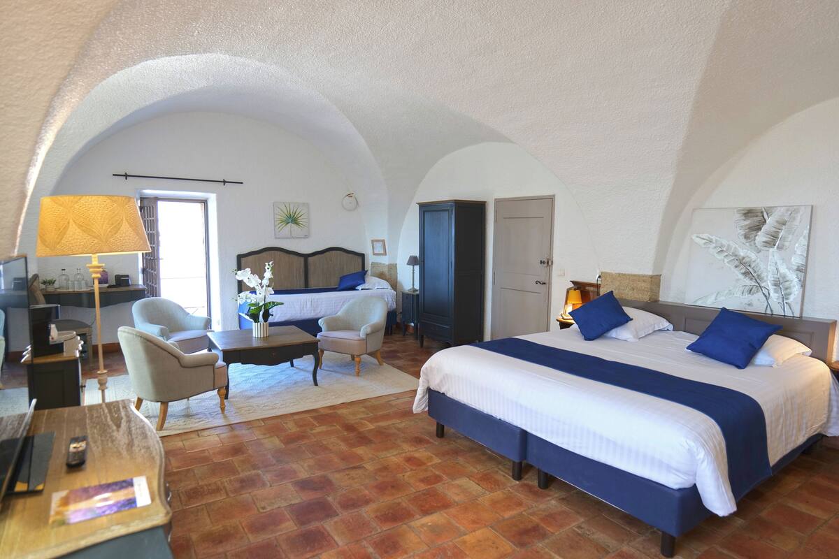 A hotel room with a large bed, two chairs, a desk, and a door.