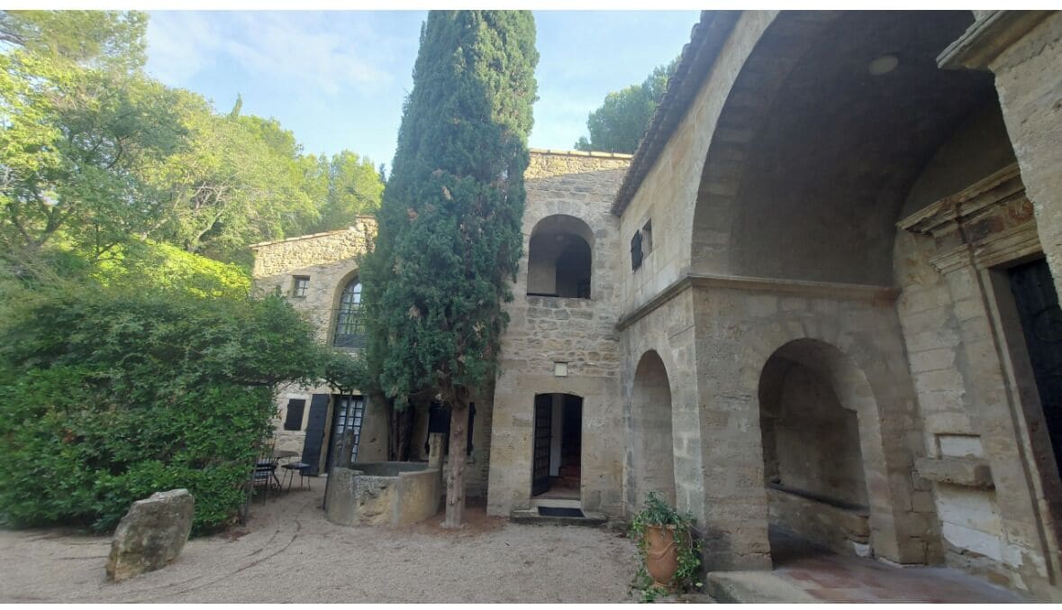 Un patio con edificios de piedra, arcos y un árbol alto.
