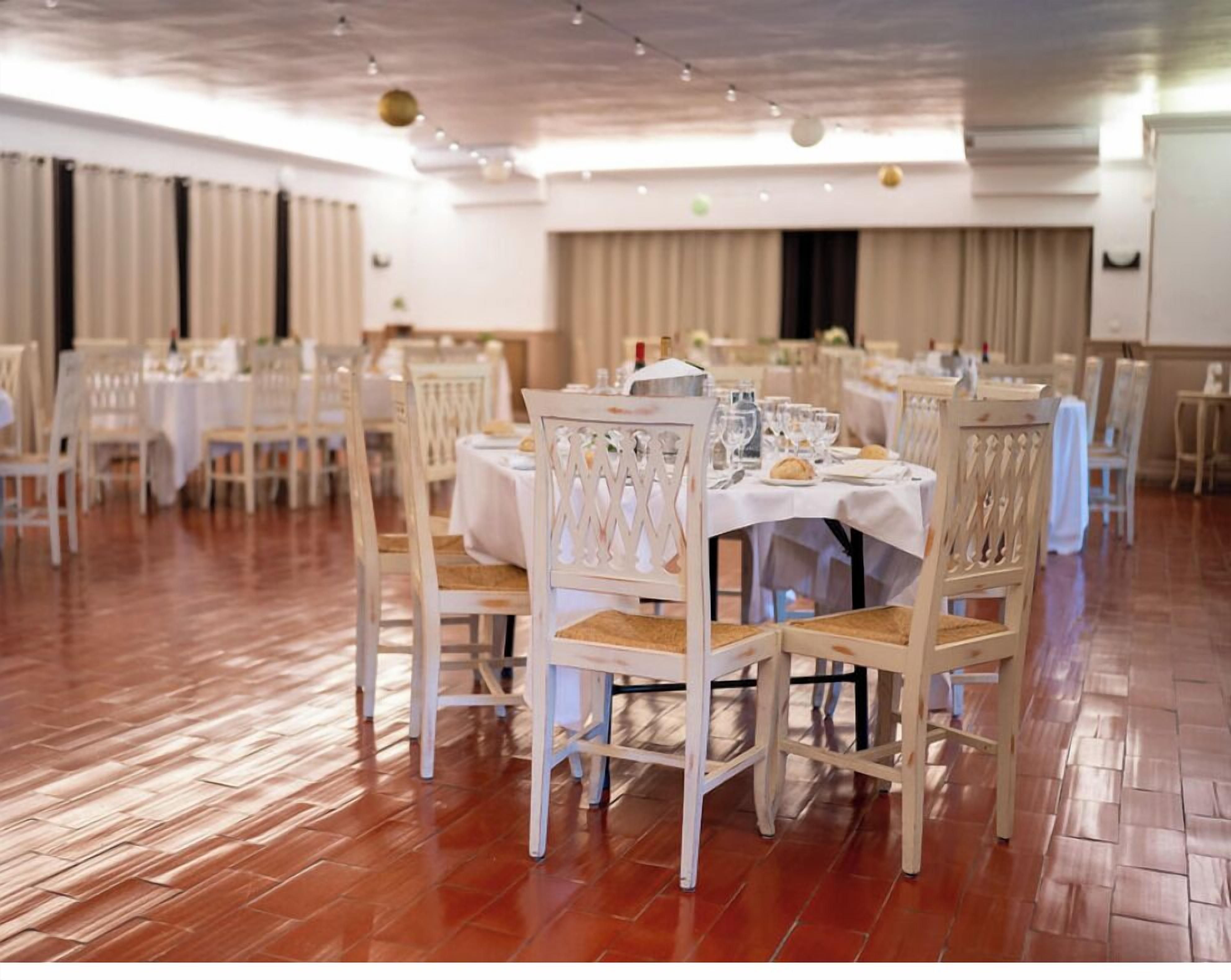 A banquet hall with round tables and white chairs, arranged in rows.