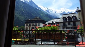Vista de la montaña con un edificio de estilo chalete en primer plano, un café con terraza y una montaña nevada al fondo.