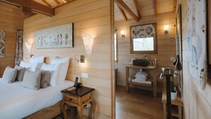 Una habitación tipo cabaña de madera con una cama, una mesita de noche y un pequeño escritorio con espejo y lavamanos.