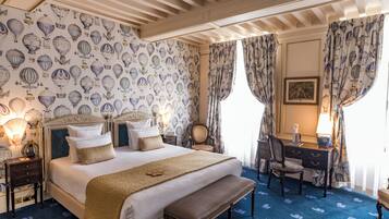 Une chambre d’hôtel avec un grand lit, un bureau et une chaise. Les murs sont recouverts d’un papier peint à motifs et le sol est recouvert d’une moquette bleue.