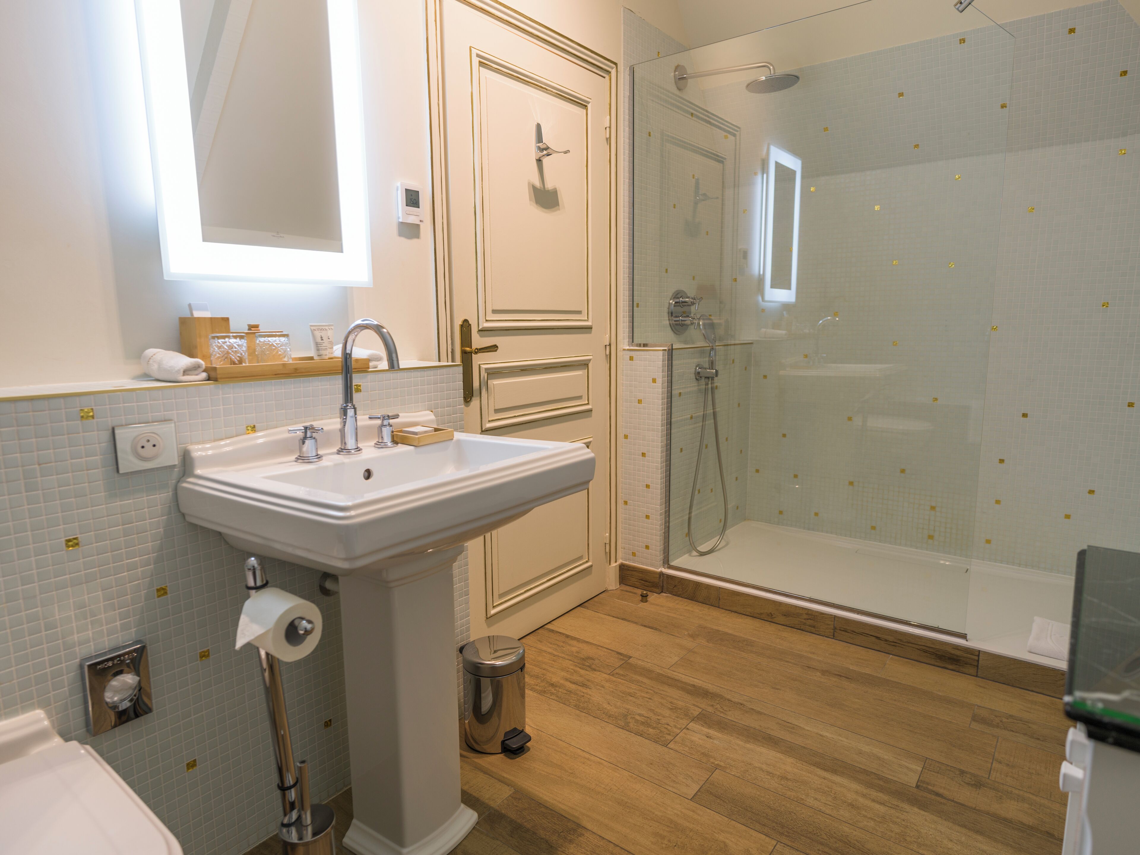 Un bagno con lavandino, specchio, doccia e pavimento in legno.