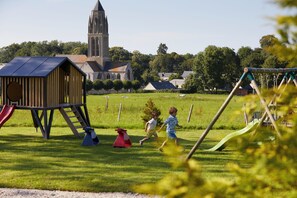 Un parque infantil con una casita de juegos de madera, toboganes y columpios.