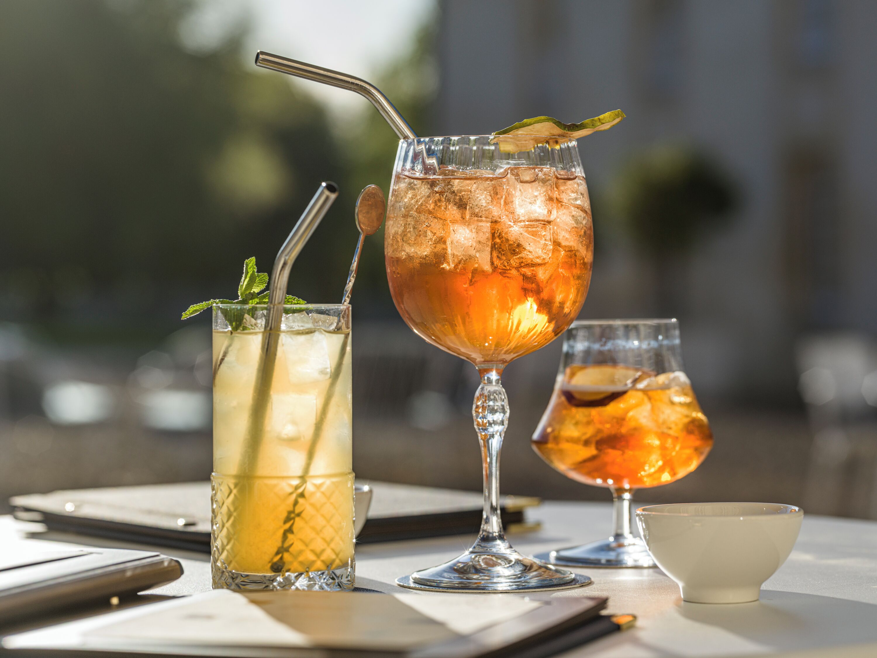 Três copos com bebidas geladas sobre uma mesa, com uma chávena e um telemóvel.