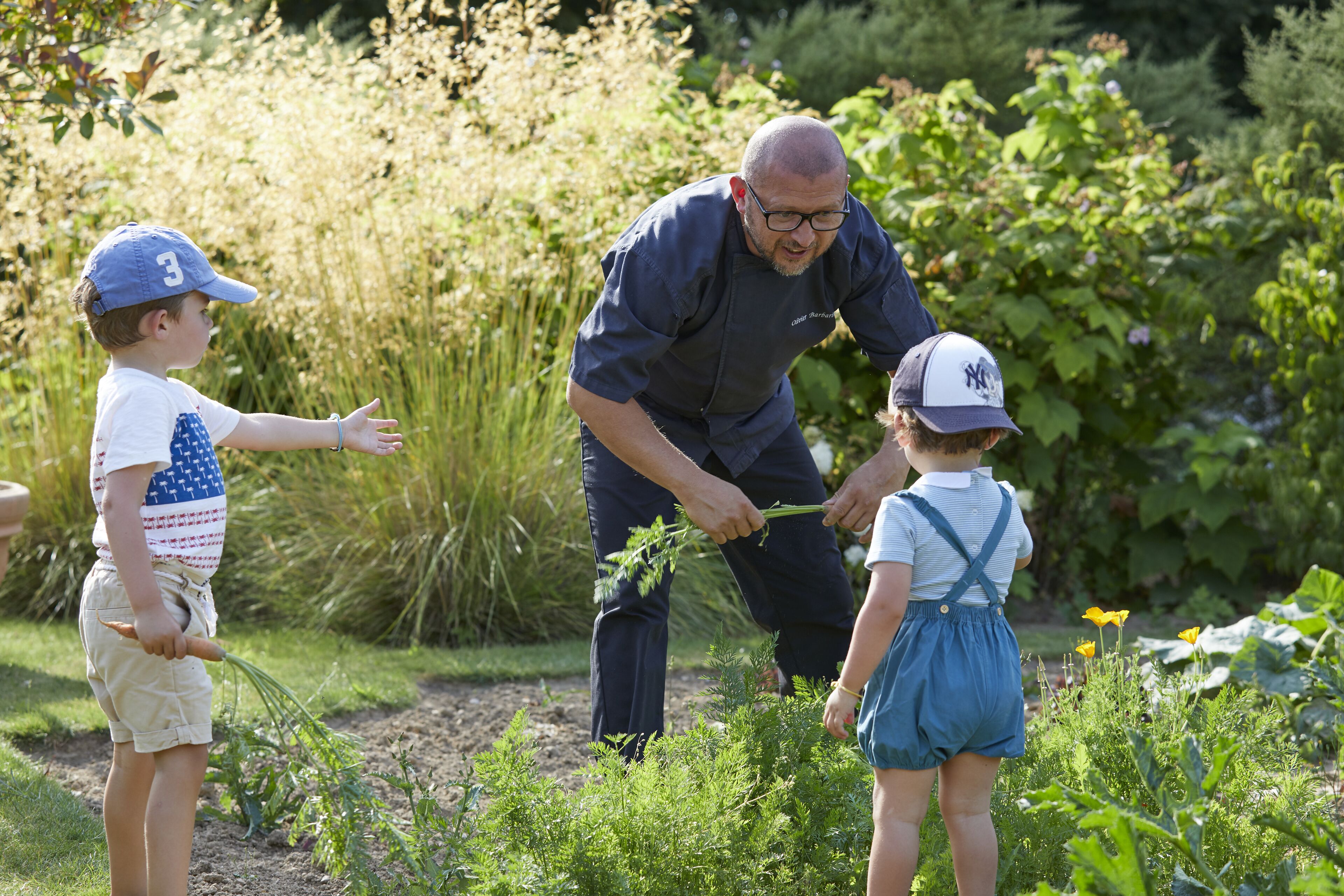 Un hombre y dos niños en un jardín, probablemente enseñándoles sobre plantas.