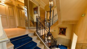 Una gran escalera con peldaños cubiertos de alfombra azul, barandillas negras ornamentadas y un candelabro.