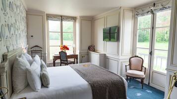 Ein stilvoll eingerichtetes Schlafzimmer mit einem großen Bett, einem Schreibtisch mit Stuhl, einem Fernseher und Blick ins Freie durch große Fenster.