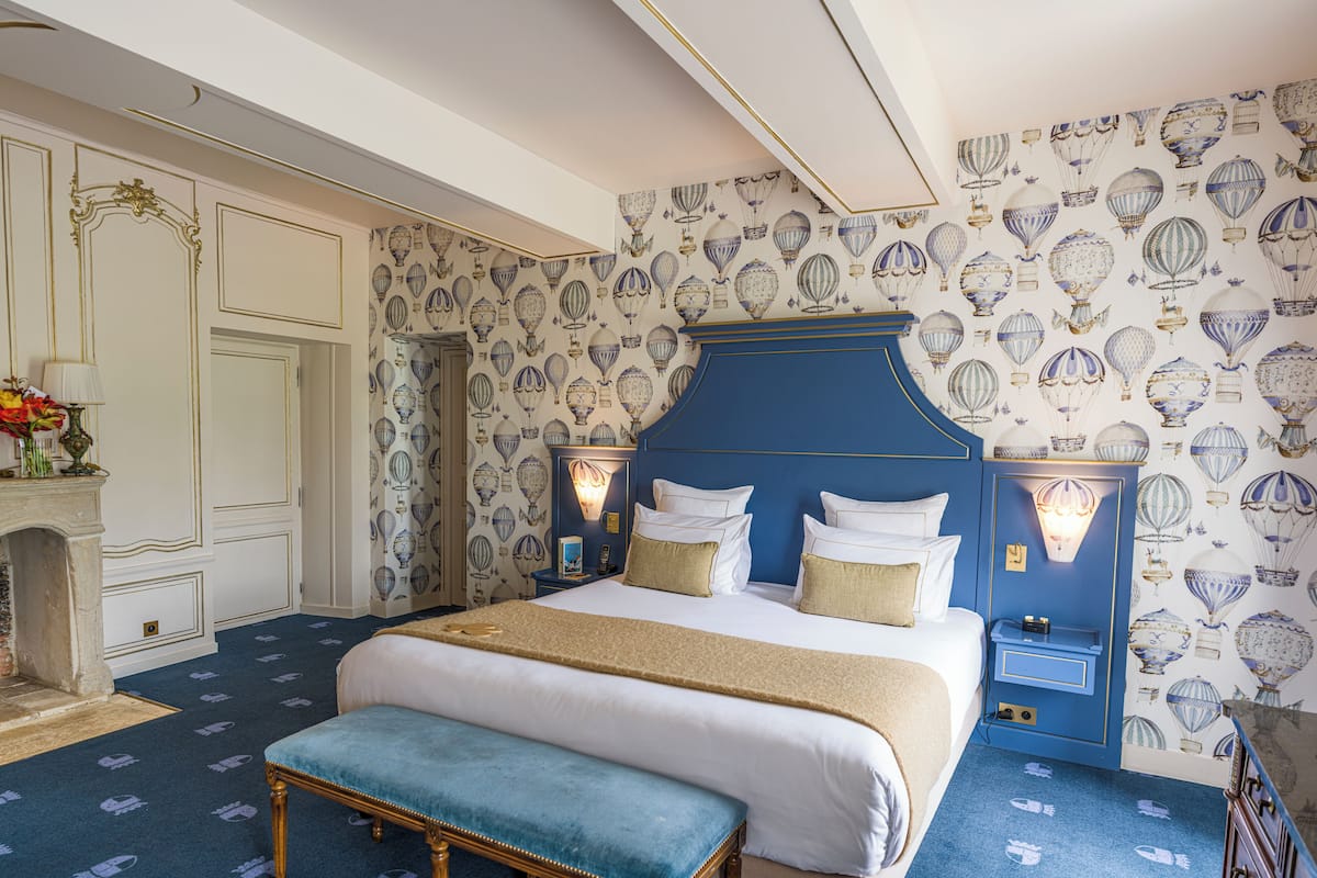 A bedroom with a large bed, a bench, a nightstand, and a wall with a hot air balloon pattern.