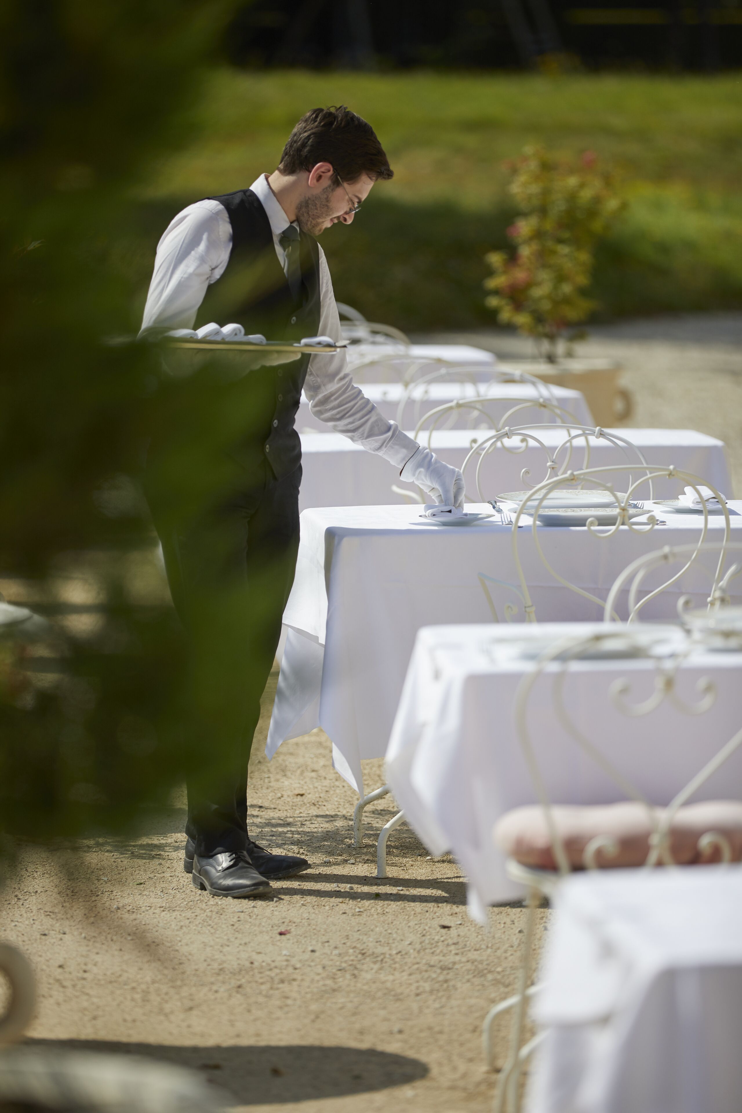 A waiter setting up a table outdoors with white tablecloths and metal wire decorations.