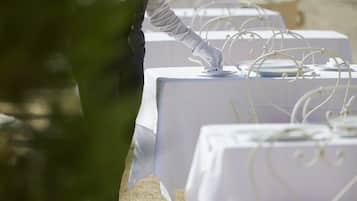 A waiter setting up a table outdoors with white tablecloths and metal wire decorations.