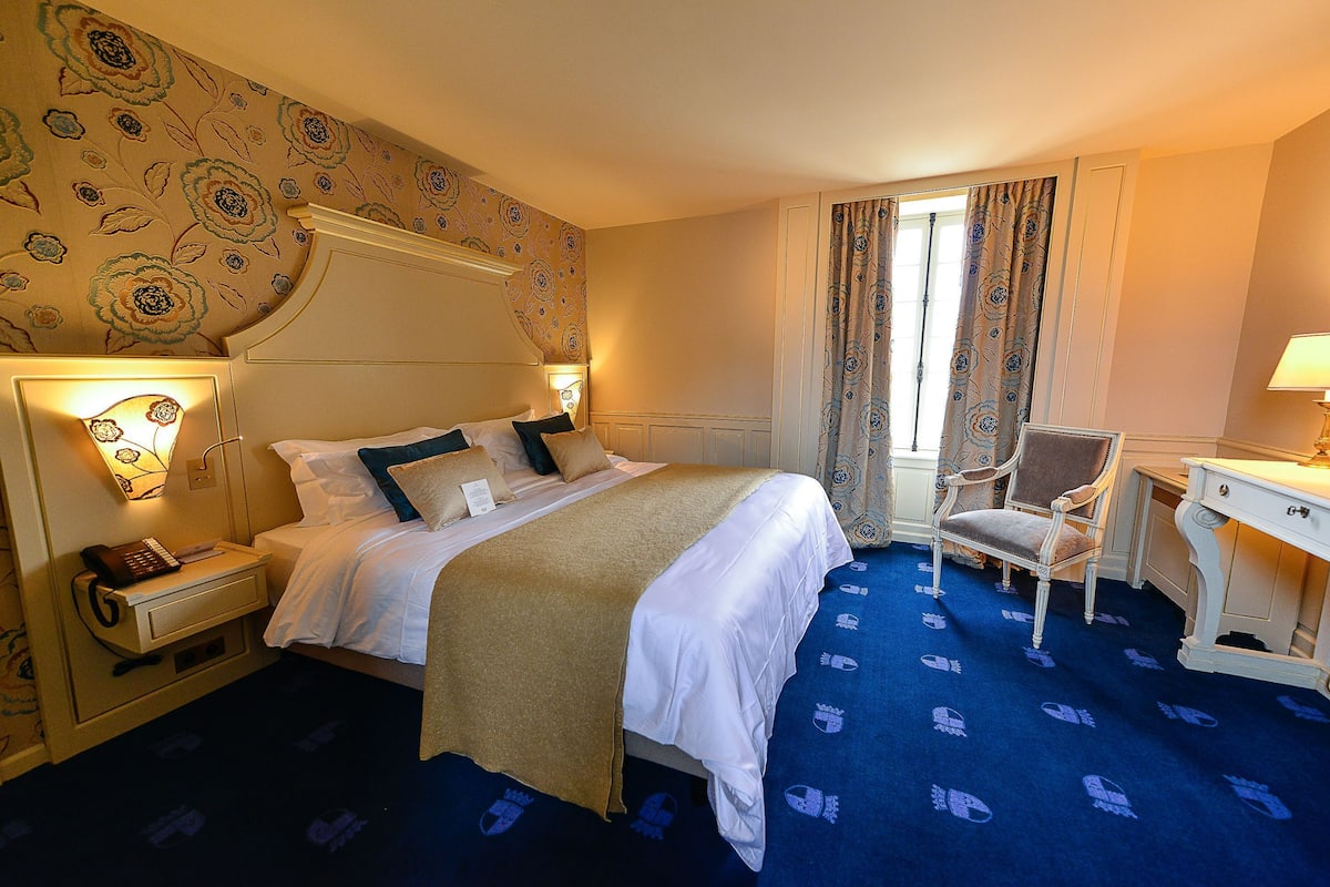 A hotel room with a bed, bedside table, chair, desk, and curtains.