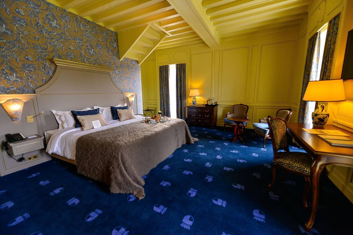 A hotel room with a bed, a desk, a chair, and a lamp.