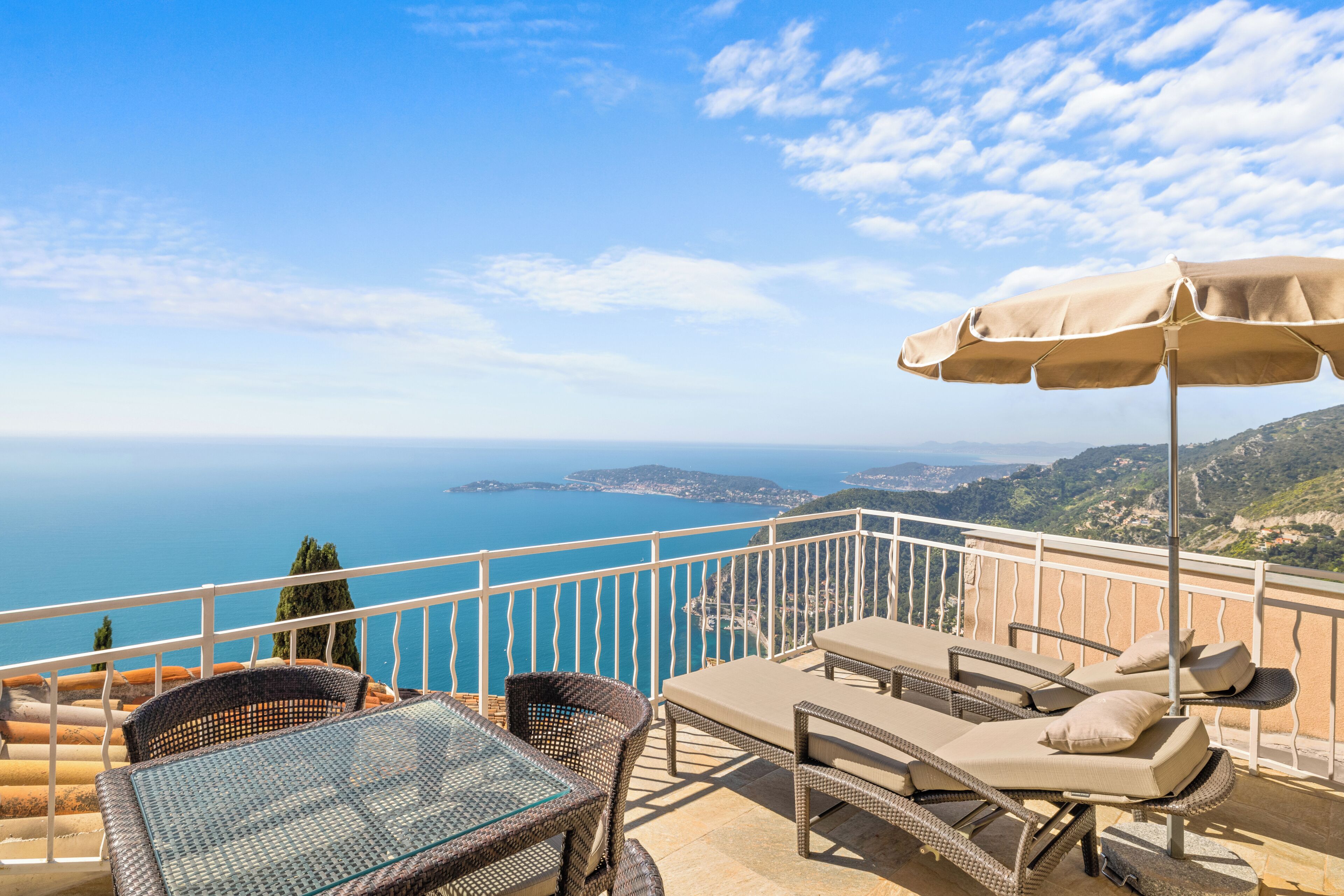 A terrace with wicker furniture, a glass table, and a view of the sea.