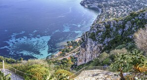 A coastal town with a steep cliff, a paved walkway, and a view of the sea.