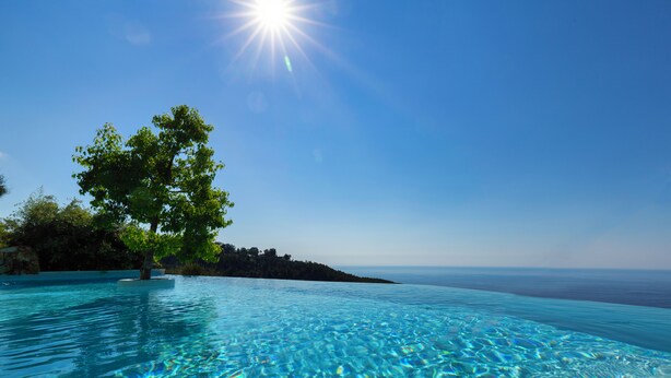 A clear blue pool with a tree on the left and a view of the ocean on the right. - Château de La Chèvre d’Or (Èze)