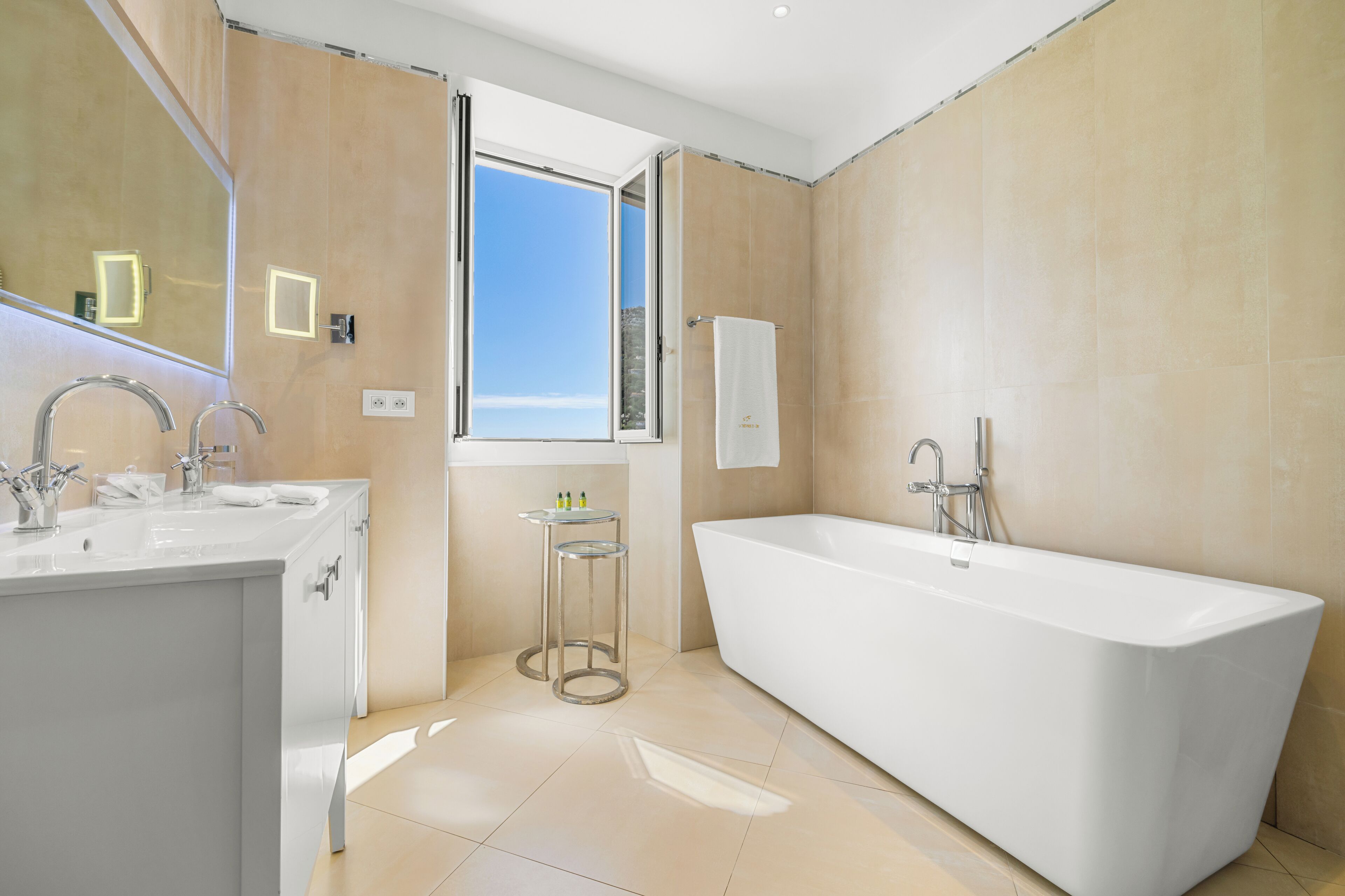 A modern bathroom with a large bathtub, two sinks, and a window providing natural light.