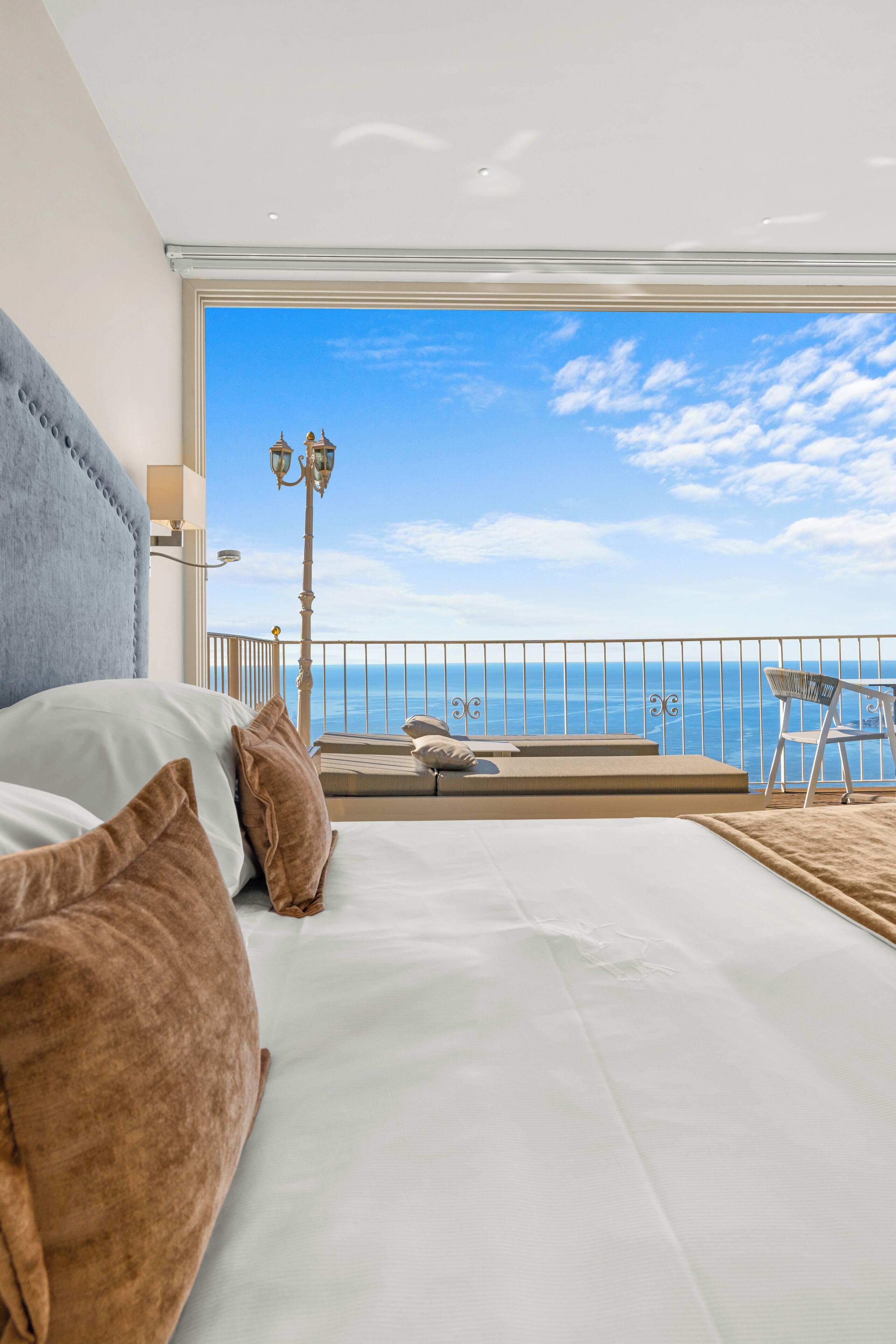 A bedroom with a large bed, a view of the sea, and a balcony with a chair and table.
