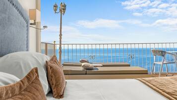 Una camera da letto con un letto grande, vista mare e un balcone con una sedia e un tavolo.