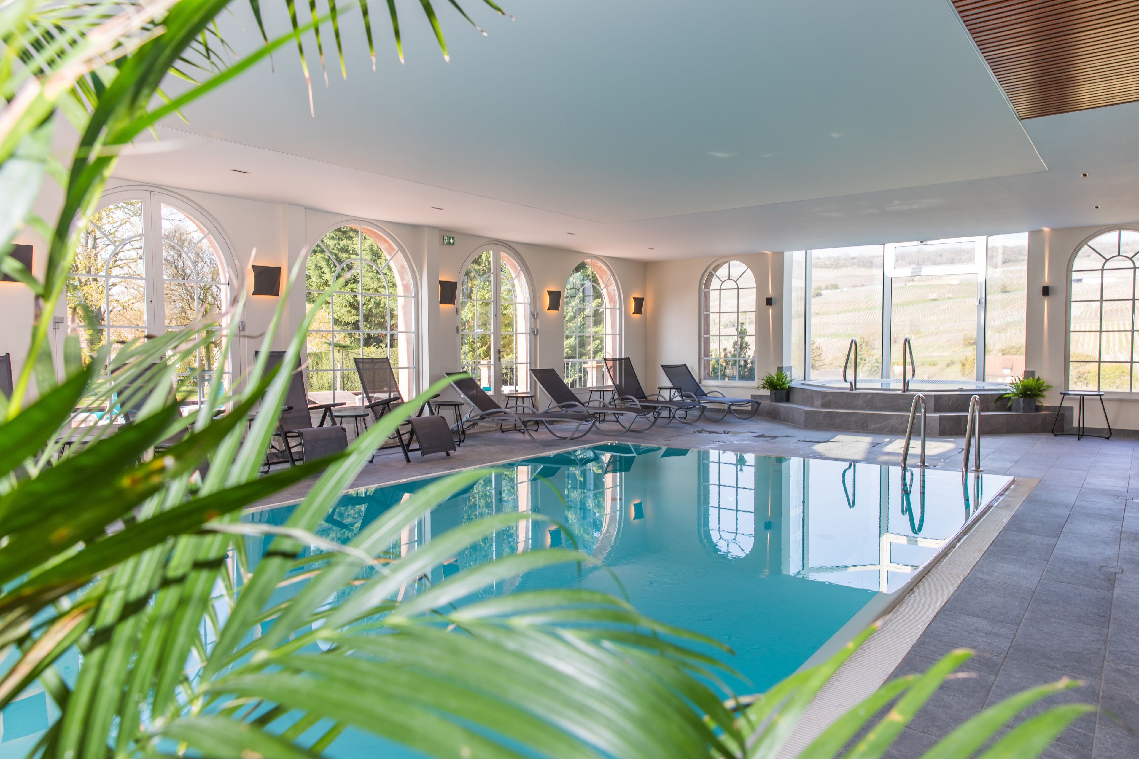 A swimming pool with lounge chairs and arched windows.