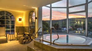 Un área de piscina interior moderna con vistas a una puesta de sol sobre un paisaje.