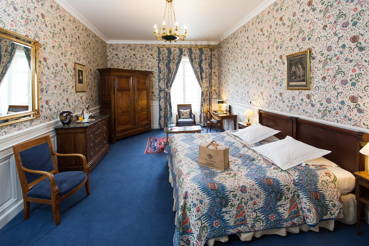 A bedroom with a large bed, a wooden dresser, a chair, and a desk.