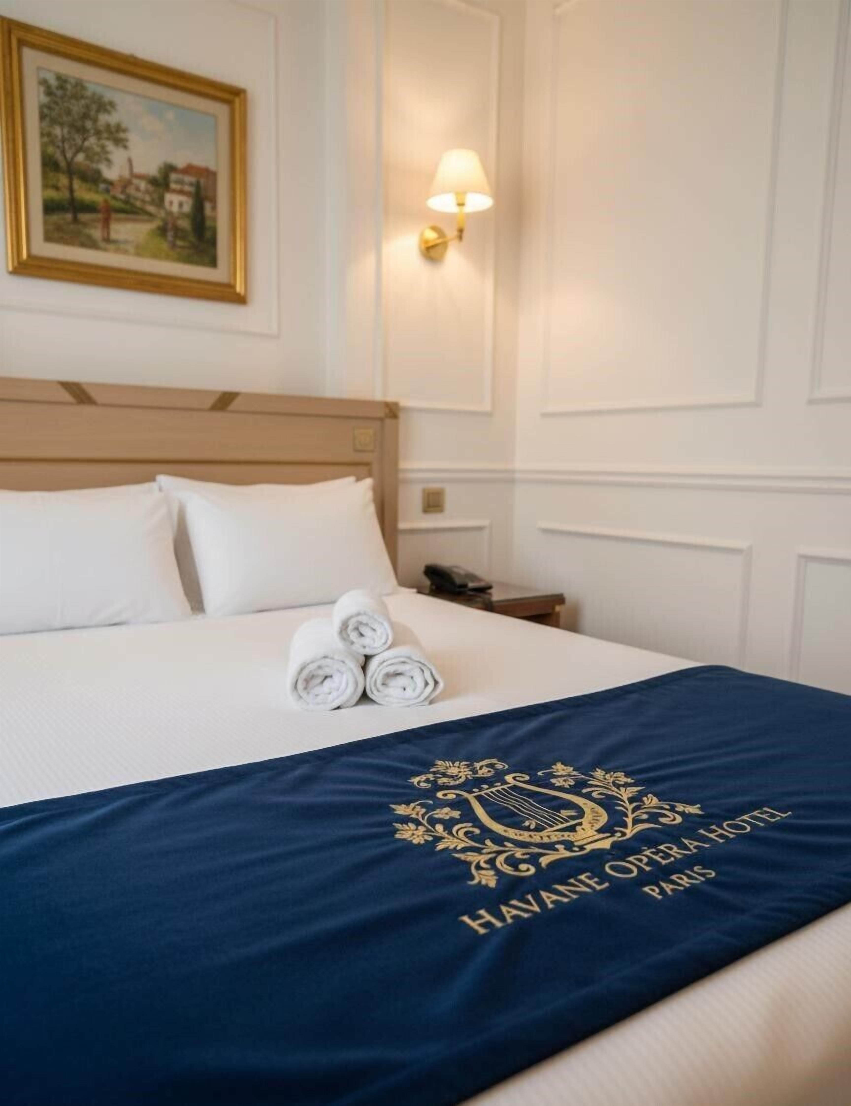 Een hotelkamer met een net opgemaakt bed, een schilderij aan de muur en een lampje op het nachtkastje.