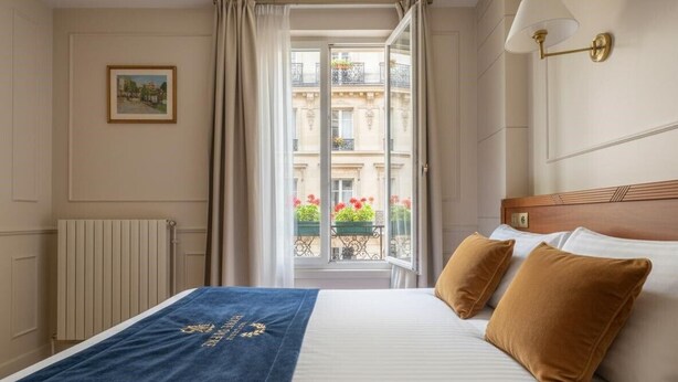 Una camera d'albergo con un letto, vista sul balcone esterno e un quadro appeso al muro.