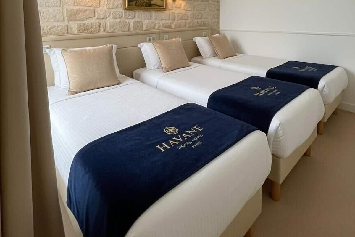 A hotel room with three beds, a stone wall, and two wall-mounted lamps.